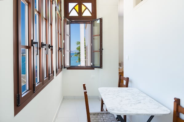 A narrow hallway with a table and chairs, a window with a view of the sea, and a door with a glass panel.
