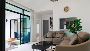 A modern living room with a glass door leading to a balcony, a sofa, a coffee table, and a wall-mounted clock. - Pool villa at Kamala Regent by Lofty (Kamala)
