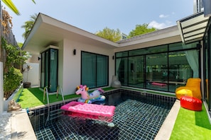A modern house with a swimming pool, a unicorn float, and a red bean bag chair.