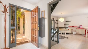 An open door leading to a balcony with a view of trees, a staircase, a white sofa, and a red accent wall. - Villa 'Del Sol' with Mountain View, Wi-Fi and Air Conditioning (Santa cristina D'aro)