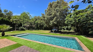 Une piscine rectangulaire à l’eau d’un bleu limpide, entourée d ’une pelouse verdoyante et bien entretenue ainsi que d’arbres.