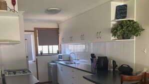 A modern kitchen with white cabinetry, a black countertop, and wooden chairs. - Quiet and comfortable 2 bedroom apartment, 65 inch Smart TV (Wodonga)