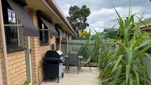 A backyard with a barbecue grill, a table, chairs, and potted plants. - Quiet and comfortable 2 bedroom apartment, 65 inch Smart TV (Wodonga)