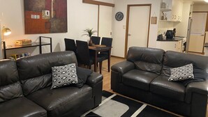 A living room with two leather sofas, a dining table with chairs, a painting on the wall, and a kitchen area visible through an open door. - Quiet and comfortable 2 bedroom apartment, 65 inch Smart TV (Wodonga)