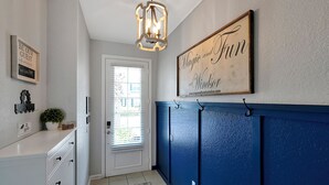 A hallway with a white door, a blue wall, and a chandelier. There are framed signs on the wall and a plant on the counter. - Home minutes to Disney with private pool, arcade, waterslides, gated resort (Kissimmee)