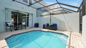 A swimming pool with a glass enclosure, a patio area with chairs and a table, and a view of the sky. - Home minutes to Disney with private pool, arcade, waterslides, gated resort (Kissimmee)