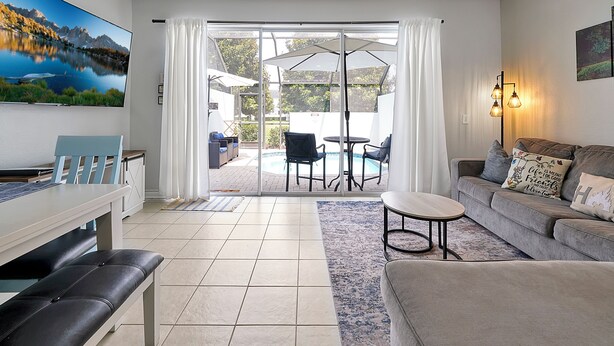 A living room with a large TV, a sofa, a bench, and a dining area with a table and chairs. - Home minutes to Disney with private pool, arcade, waterslides, gated resort (Kissimmee)