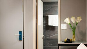 Een moderne badkamer met een marmeren wand, een glazen douchecabine en een klein tafeltje met een bloevas.