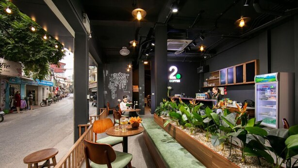 Een caféruimte met houten meubels, een groene, beklede bank en diverse planten.