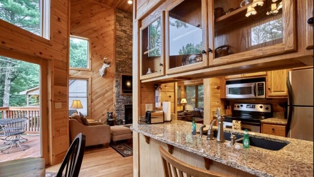 A wooden cabin interior with a kitchen featuring granite countertops, stainless steel appliances, and wooden cabinets. - Mountain Memories - Cabin near Blue Ridge Parkway (Boone)