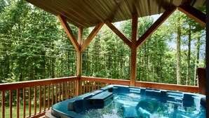 A hot tub under a wooden deck with a forest view. - Mountain Memories - Cabin near Blue Ridge Parkway (Boone)