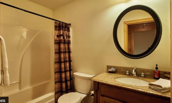 A bathroom with a shower, toilet, sink, and mirror.