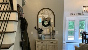 A living room with a wooden bench, a white cabinet with decorative items, a mirror with a wreath, and a sign reading "GARDEN" in the background. - •Treehouse by The Lake• (Chattanooga)