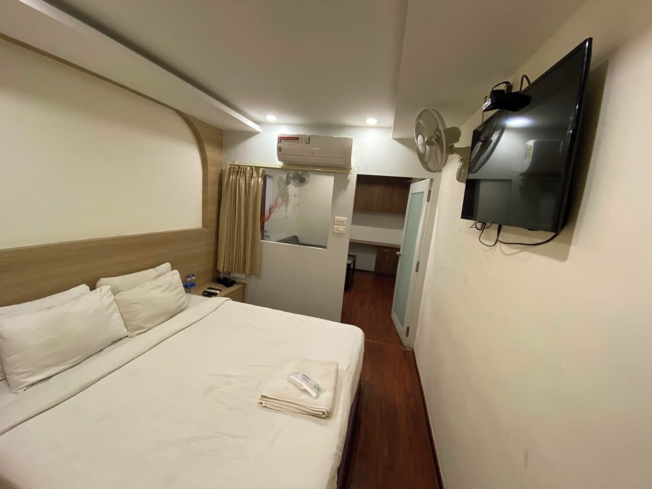 Una habitación de hotel con cama, televisión montada en la pared, aire acondicionado y ventilador.