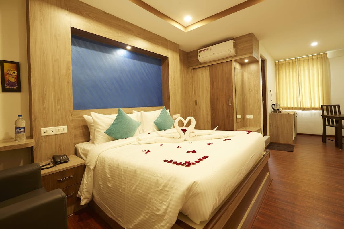 A hotel room with a large bed, a desk, a chair, a wardrobe, and an air conditioning unit.