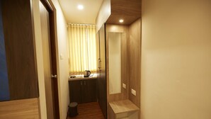 Un pasillo estrecho con piso de madera, un cubo pequeño de basura y una kitchenette con un lavamanos y una tetera.