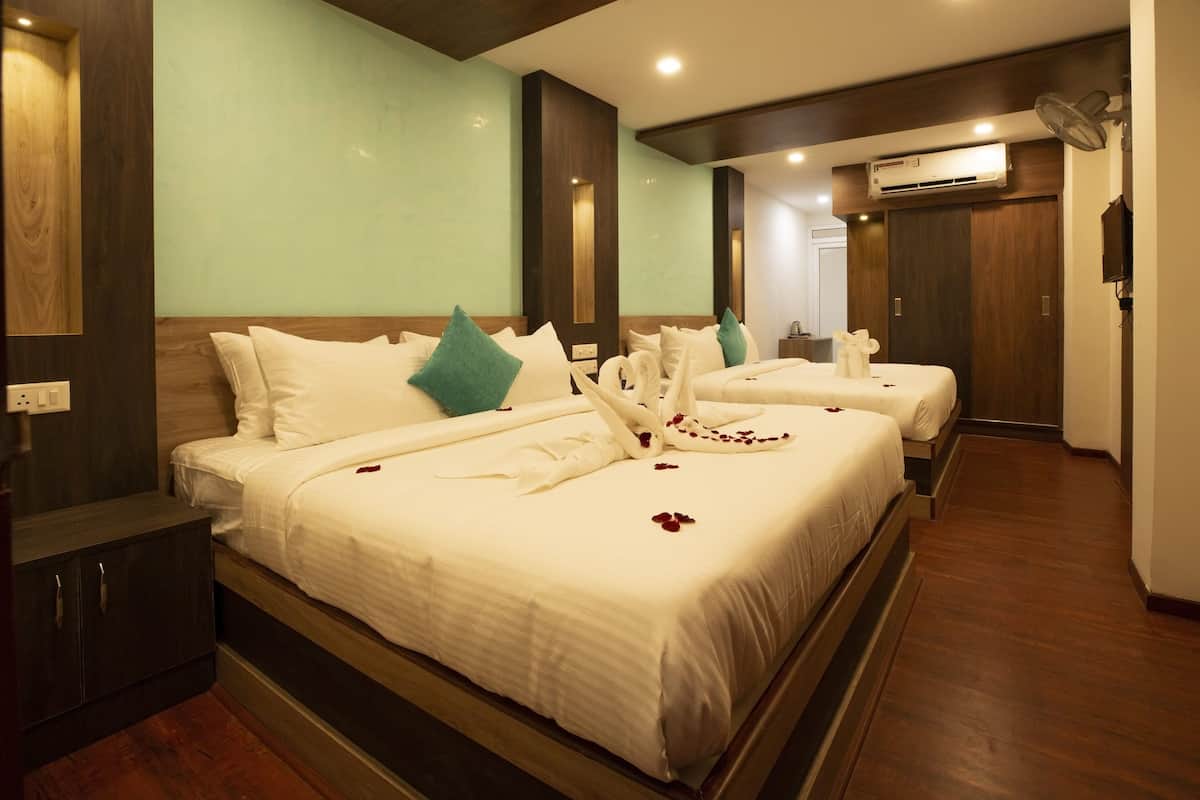 A hotel room with a large bed, a smaller bed, a wardrobe, and an air conditioning unit.
