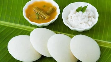 Ein Teller Idlis mit einer Schüssel Kokosnuss-Chutney und Sambar, sowie eine Schüssel Kokosraspeln auf einem Bananenblatt.