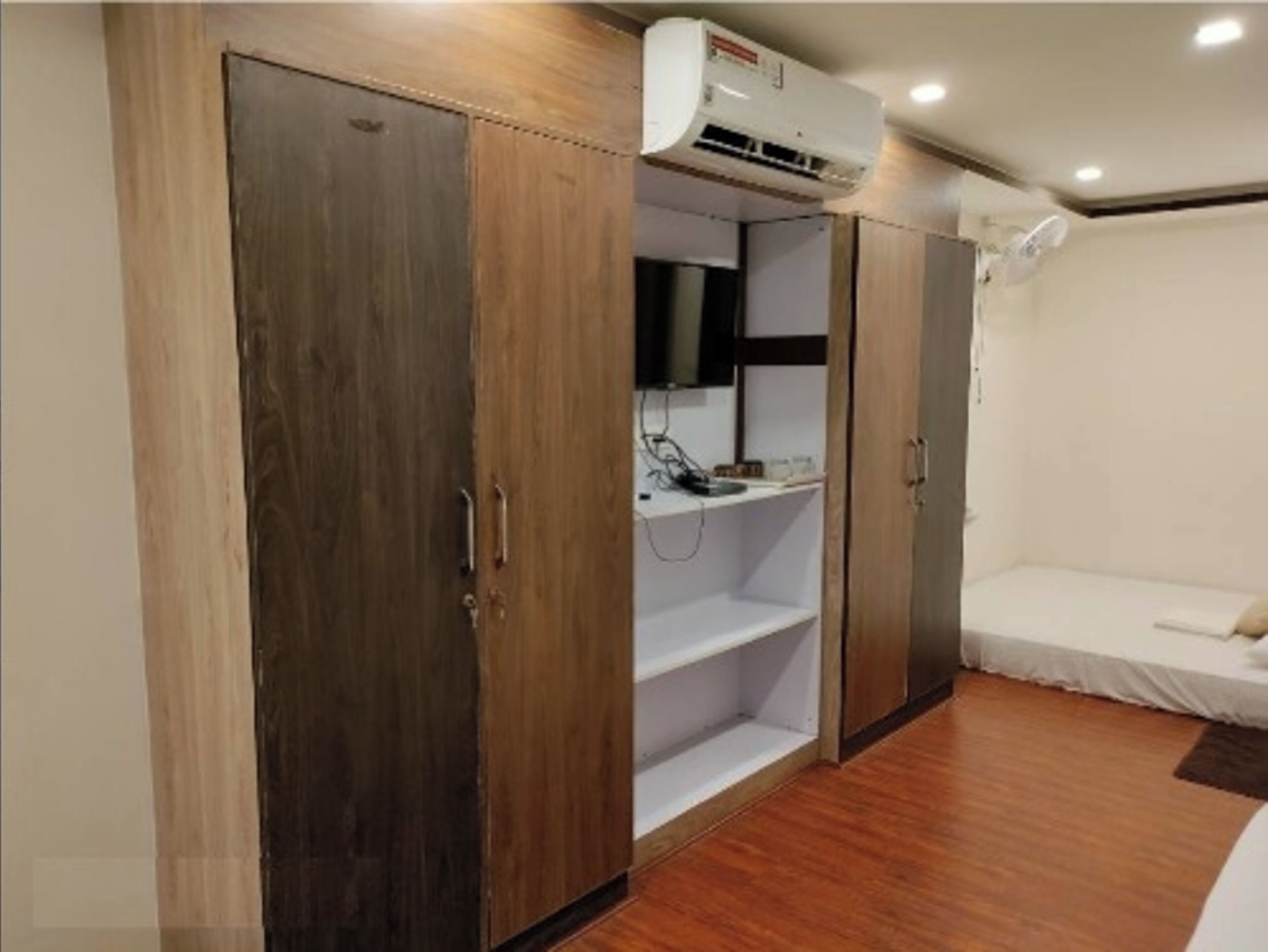 A bedroom with a wardrobe, a bed, an air conditioning unit, and a bedside table.