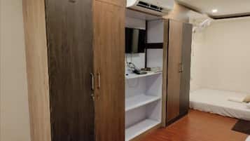 A bedroom with a wardrobe, a bed, an air conditioning unit, and a bedside table.