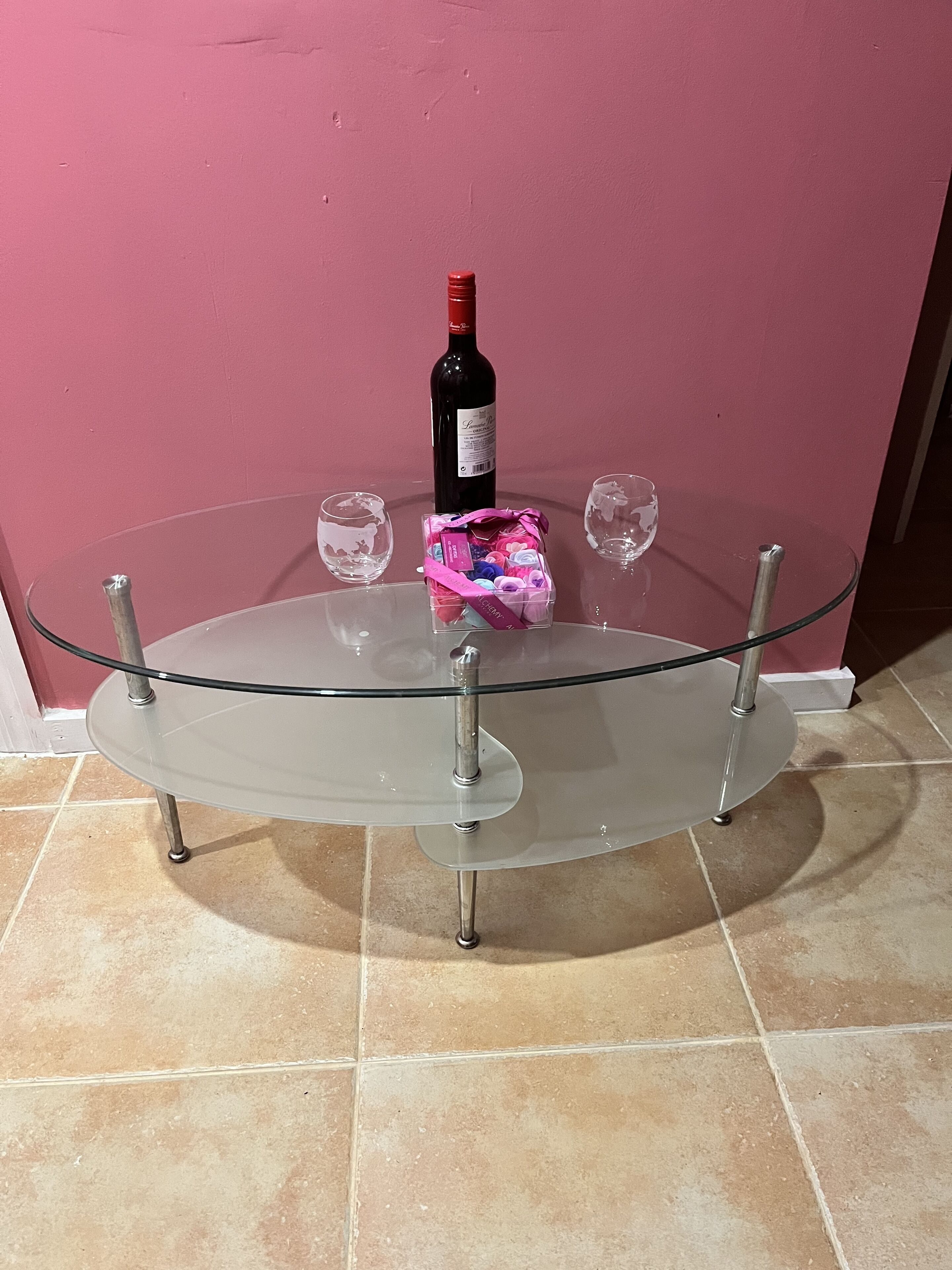 Een tafel met glazen blad, een wijnfles en een geschenkmand.