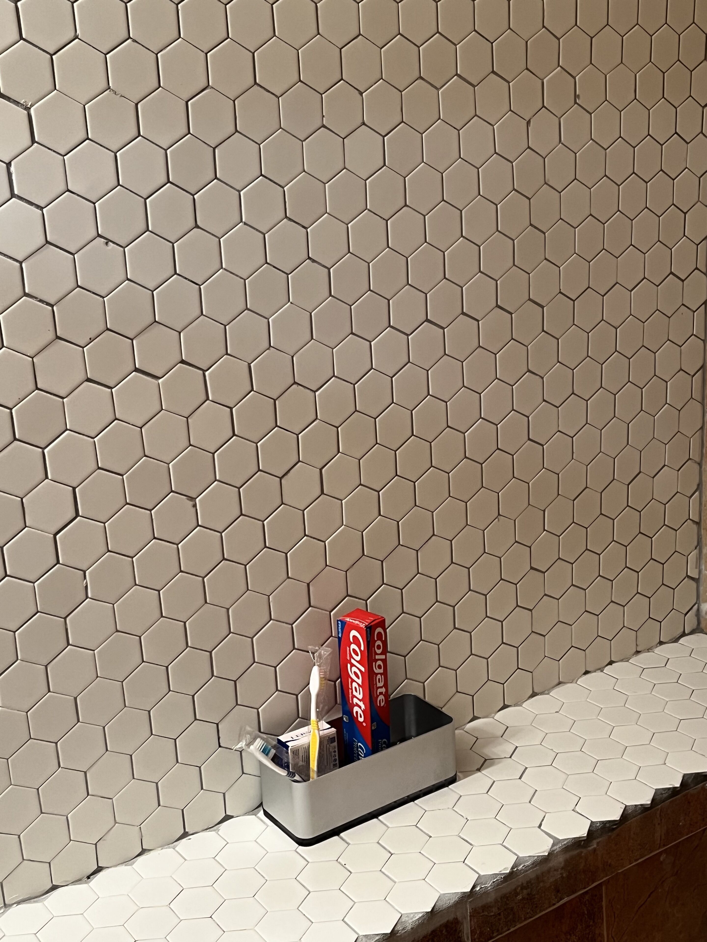 Et badeværelse med sekskantede fliser i et beige mønster, en tandbørste, tandpasta og en dåse Coca-Cola i en holder på bordet.