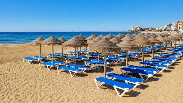 A beach with rows of blue lounge chairs and thatched umbrellas. - Apt  near center & port (Torrevieja)