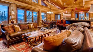 A log cabin interior with a large dining table, leather sofas, and a view of the mountains through large windows. - STUNNING custom log home, 4 en-suites, amazing views, hot tub, pool table! (Breckenridge)