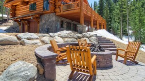 A log cabin with a stone foundation, wooden deck, and outdoor seating area with Adirondack chairs. - STUNNING custom log home, 4 en-suites, amazing views, hot tub, pool table! (Breckenridge)