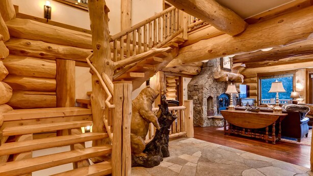 A log cabin interior with a wooden staircase, a stone fireplace, and a dining area with a table and chairs. - STUNNING custom log home, 4 en-suites, amazing views, hot tub, pool table! (Breckenridge)
