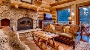 A log cabin interior with a stone fireplace, leather sofa, and a television. - STUNNING custom log home, 4 en-suites, amazing views, hot tub, pool table! (Breckenridge)