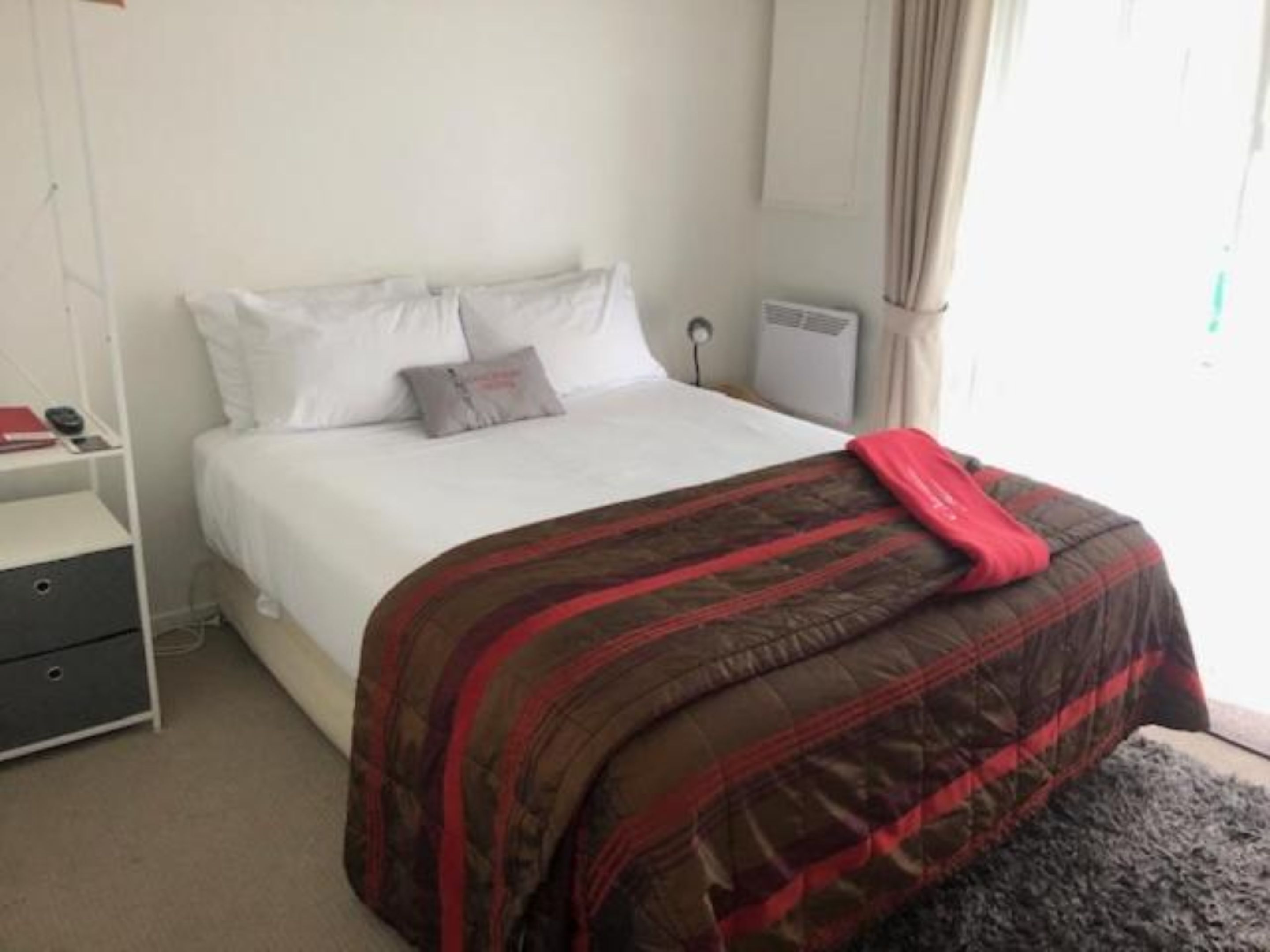 A bedroom with a bed, a bedside table, a lamp, and a window with curtains.