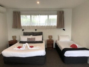 A hotel room with two beds, a window with curtains, a bedside table with a lamp, and a wall-mounted phone.