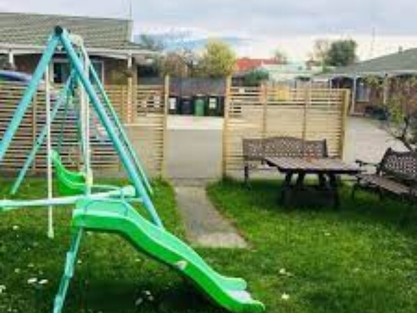 A playground with a green slide and swings, a picnic table, and a fence.