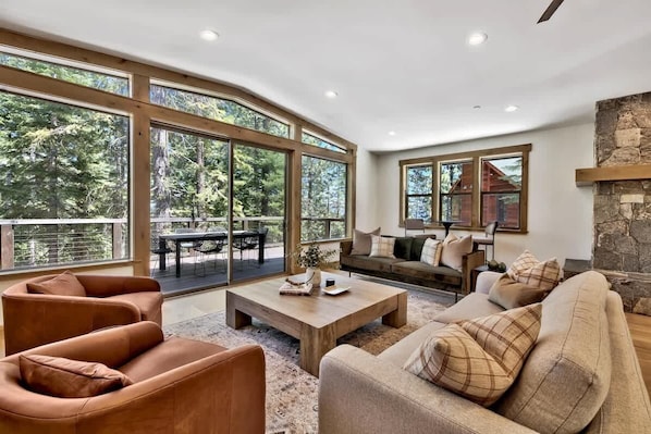 A spacious living area with large windows, a stone fireplace, and a cozy seating arrangement. - Treetops Designer Lodge: Air Conditioning, Hot Tub (Tahoe Vista)