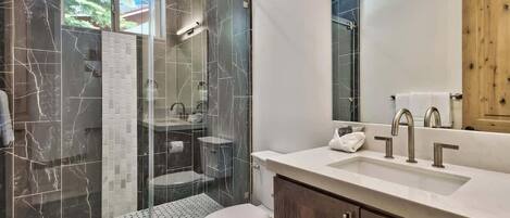 A modern bathroom with a glass-enclosed shower, a white toilet, and a vanity with a mirror and sink.