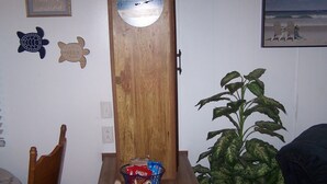 A room with a wooden door, a wall clock, a welcome sign, a chair, a plant, and a framed picture.