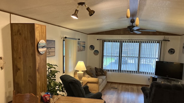 A cozy living room with a wooden floor, a sofa, a chair, a TV, and a window with blinds.