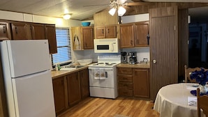 A compact kitchen with wooden cabinets, a white refrigerator, a microwave, a stove, and a sink.