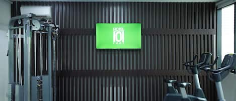 Un gimnasio con máquinas de pesas, cintas de correr y una televisión que muestra