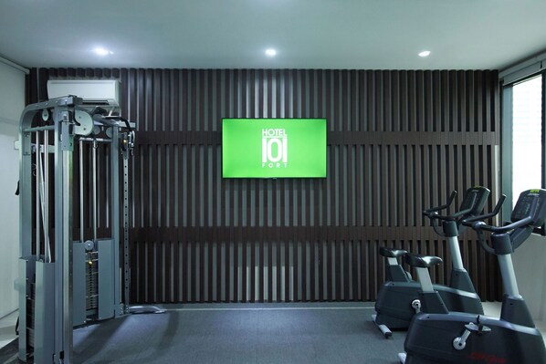 Un gimnasio con máquinas de pesas, cintas de correr y una televisión que muestra