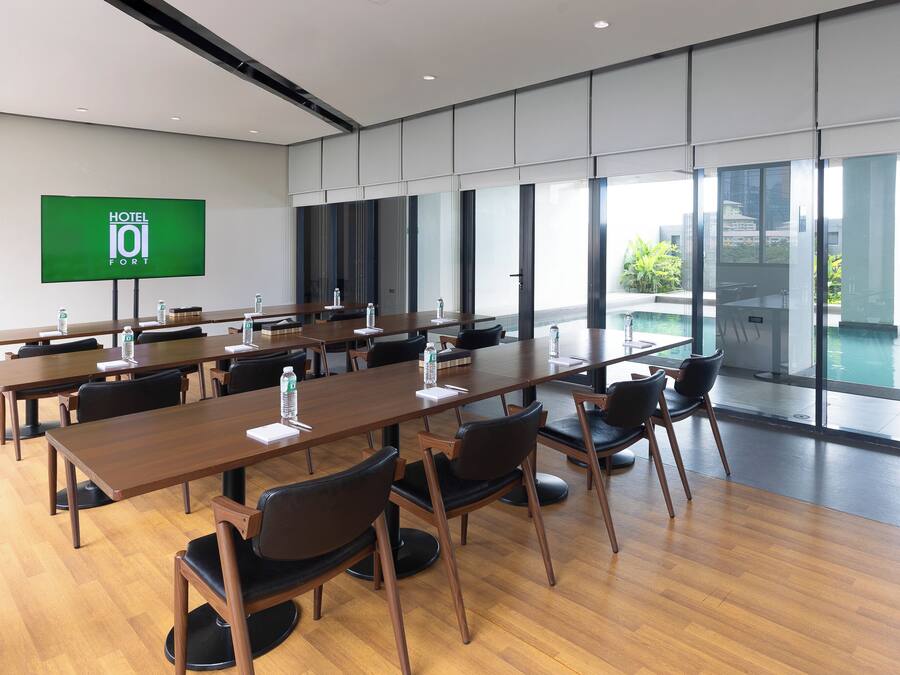 Una sala de conferencias moderna con largas mesas y sillas, una pantalla grande que muestra 'HOTEL 101 FORT', y amplias ventanas con vistas al exterior.