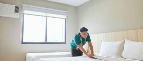A hotel room with a large bed, a smaller bed, a window with blinds, and an air conditioning unit on the wall.