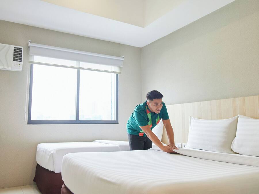 Une chambre d’hôtel avec un grand lit, un lit plus petit, une fenêtre avec des stores et un climatiseur fixé au mur.