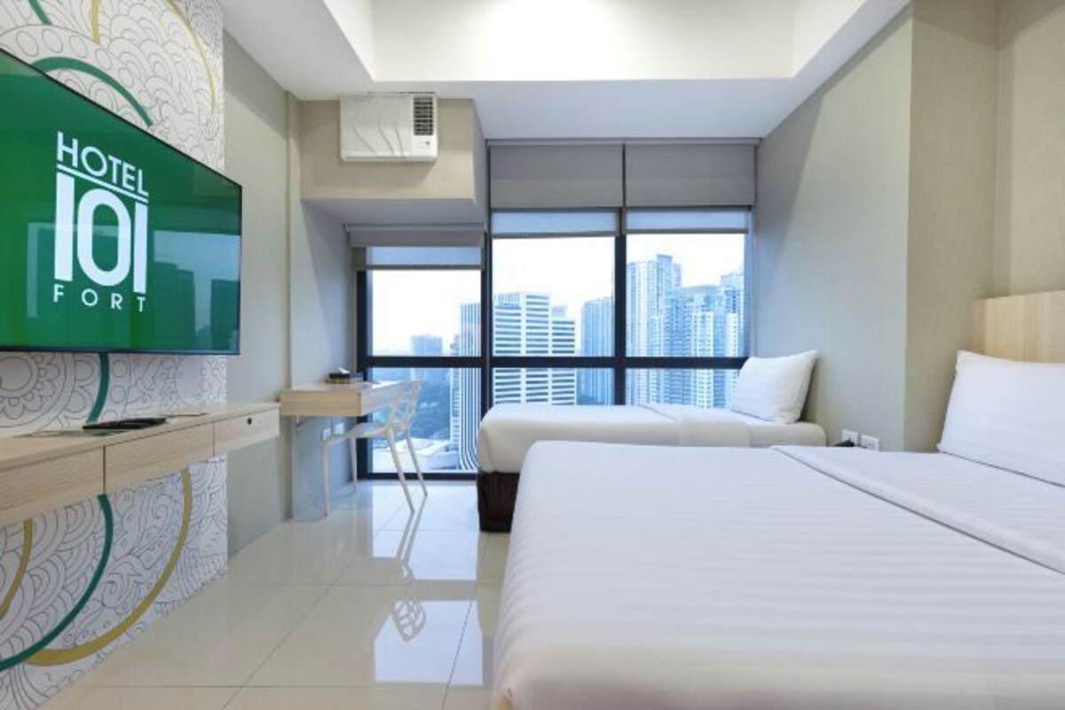 Una habitación de hotel con un ventanal grande, una cama, un escritorio y un televisor.