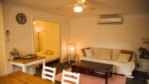 Una sala de estar acogedora con una mesa de madera, sillas blancas, un sofá y un ventilador de techo.