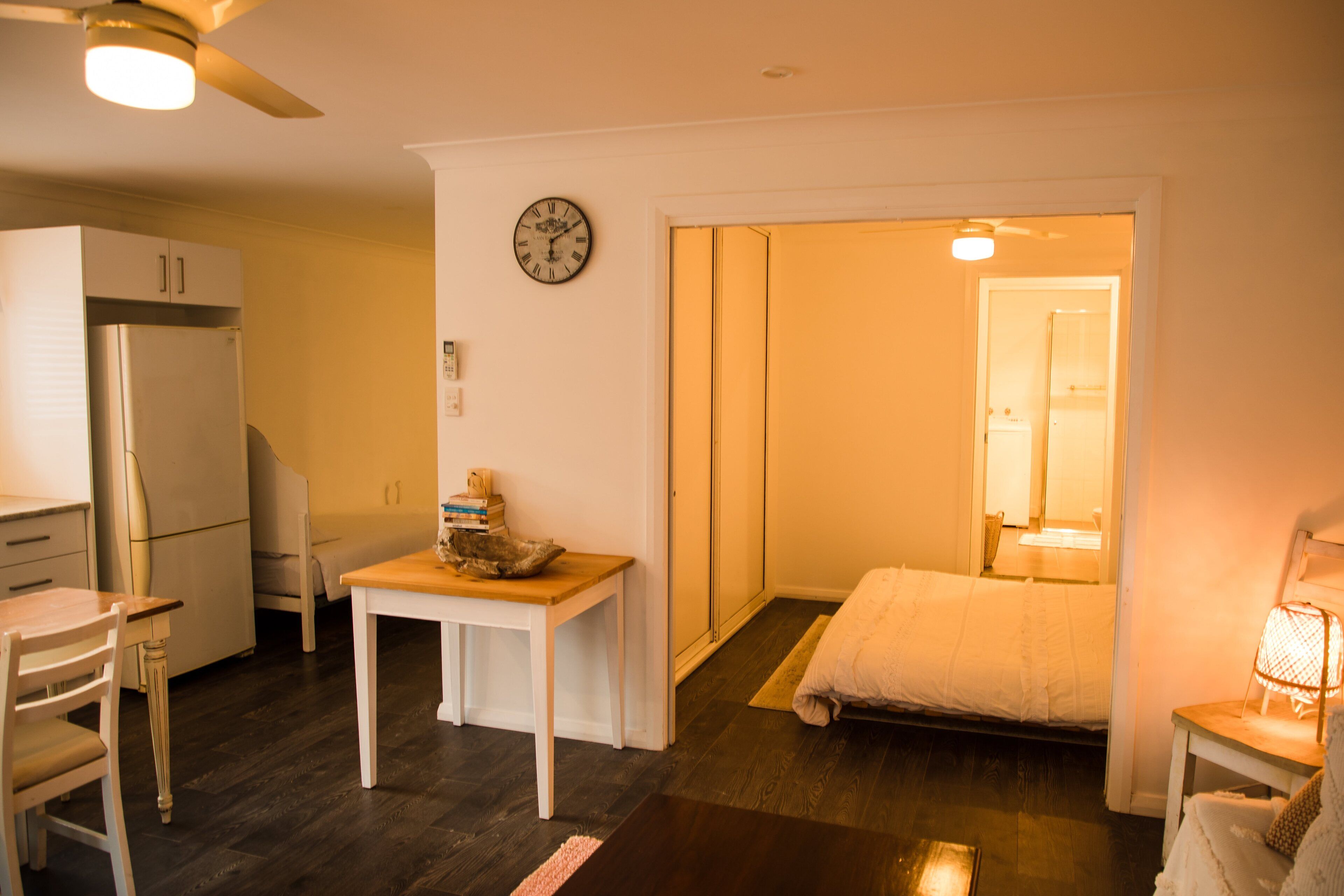 A compact living space with a kitchenette, a dining area, a bed, and a small table with a lamp.