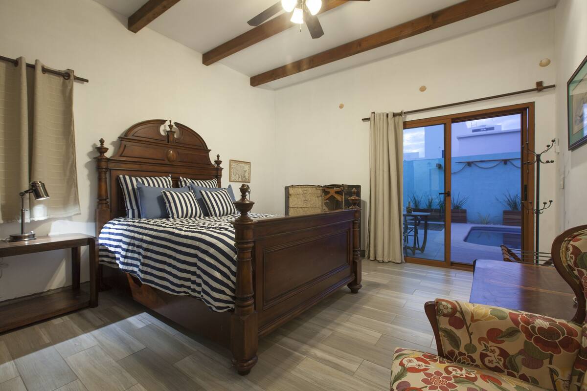 A bedroom with a wooden bed, a nightstand, a chair, and a view of the outside through a sliding glass door.