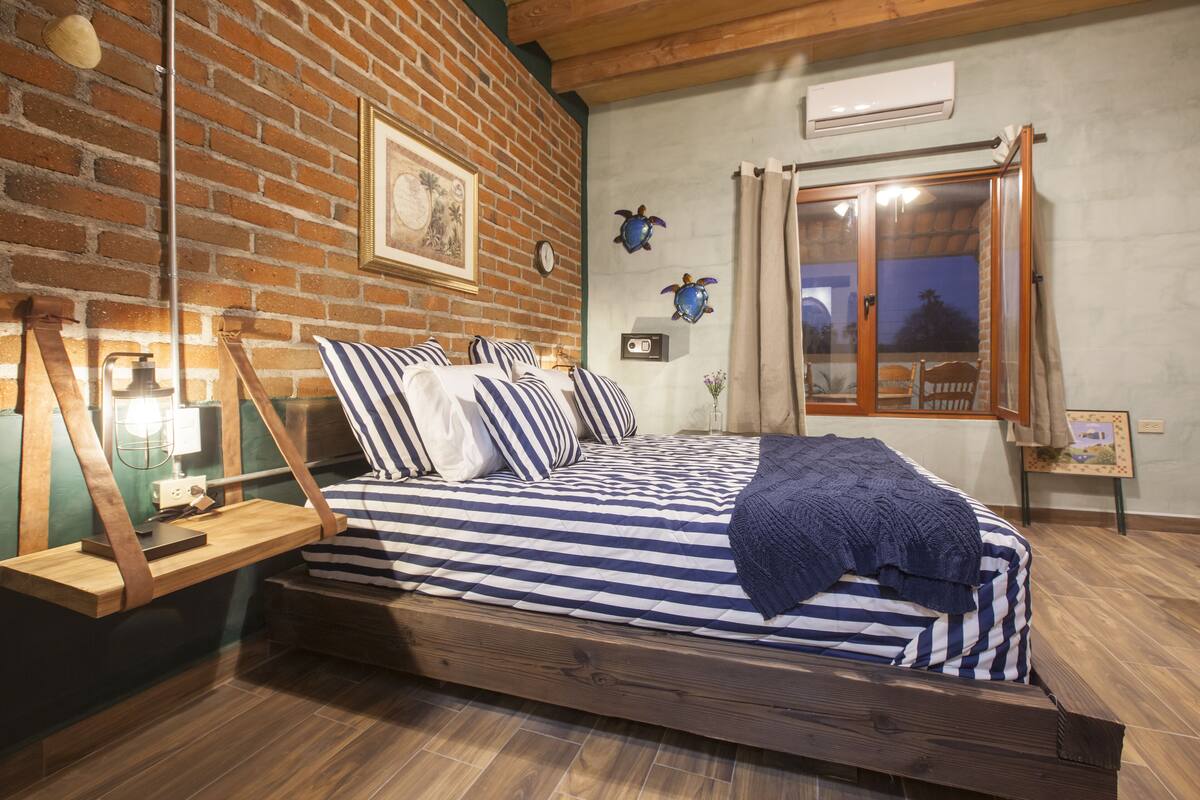 A bedroom with a wooden bed, striped bedding, a brick wall, and a window with curtains.
