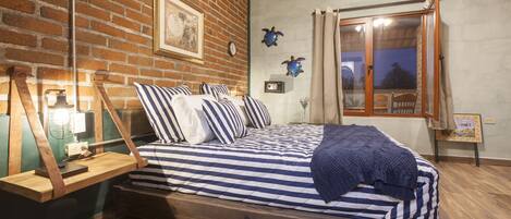 A bedroom with a wooden bed, striped bedding, a brick wall, and a window with curtains.